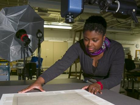 A woman adjusts a paper document below a camera in preparation for its picture to be taken